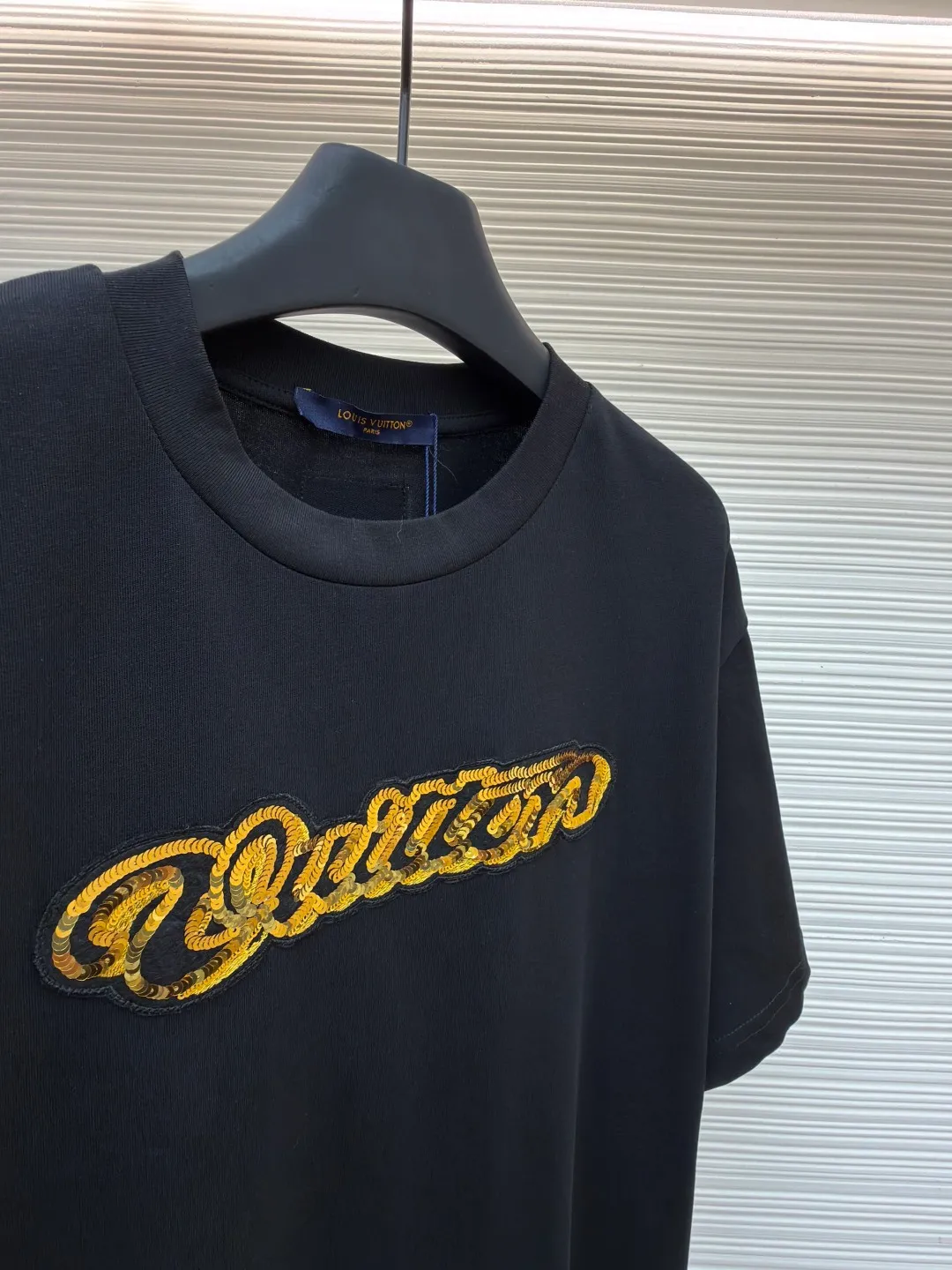 LOUIS VUITTON cotton round neck embroidered Vuitton signature logo short sleeves ●Original version: purchased and developed for 12300 ●Item number: 1682273-A10 ●Fabric: cotton fabric ●Technology: embroidery production ●Color: black ●Version: fitted version ●Weight: about 295 grams ●Size: S-M-L-XL ●Description: This white short-sleeved T-shirt is made of high-count combed cotton fabric and has been treated with pre-washing technology. It has a soft and skin-friendly touch and is not easy to deform. The silhouette of the shirt is a loose shoulder design, which meets the needs of modern casual wear. The core decoration area on the chest uses hand-beading and bronzing technology, and uses metallic gold sequins and embroidery threads intertwined to outline a three-dimensional letter pattern. The sequins are layered and inlaid, and each one is manually positioned and fixed by craftsmen to ensure a regular texture and uniform gloss. The edges of the letters are sewn with matte silk thread to form a visual contrast between gold and matte, while reinforcing the decorative structure to avoid falling off during wear. The neckline uses double-needle hemming technology and is matched with ribbed cuffs of the same fabric. It is durable and fits the neck. The overall craftsmanship combines handicraftsmanship with modern clothing technology, and the details show exquisite texture. The overall wiring is straight and delicate, the fabric is comfortable and soft, and the color is consistent without color difference. It can be matched with the same style to create a fashionable look and control various occasions. Customized accessories, complete with three standards, same style for men and women!